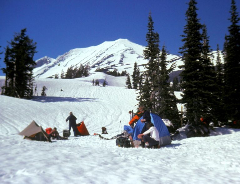 Mountain climbers set up camp on a snowfield below the snowy cone of Mt Adams