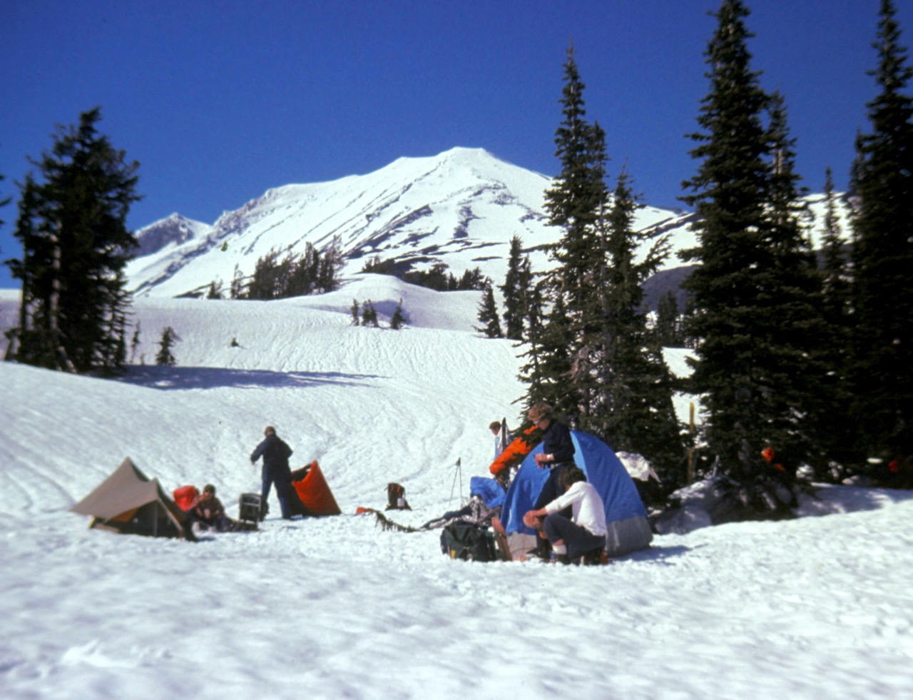 Mountain climbers set up camp on a snowfield below the snowy cone of Mt Adams
