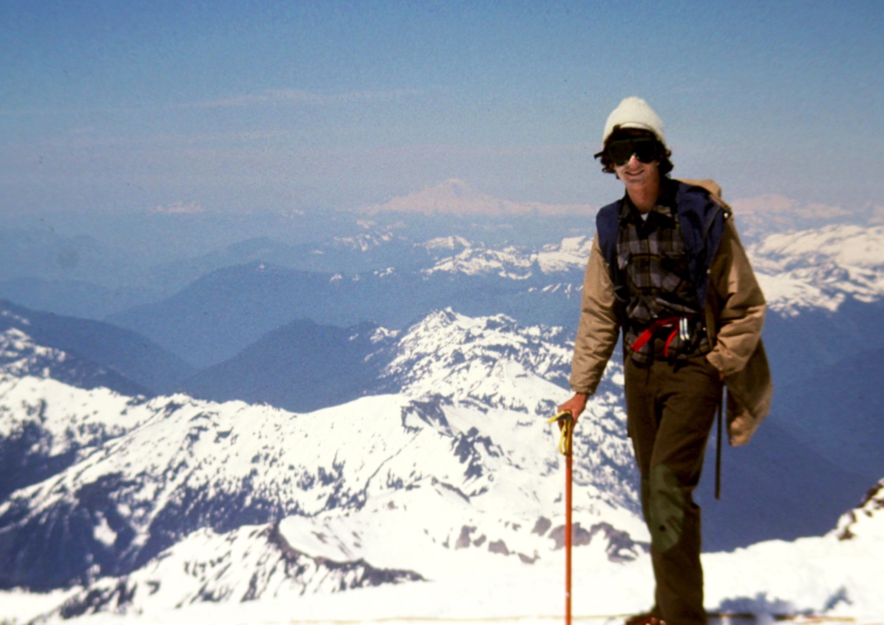 Young mountain climber on the summit of Glacier Peak with snowy mountains in the background