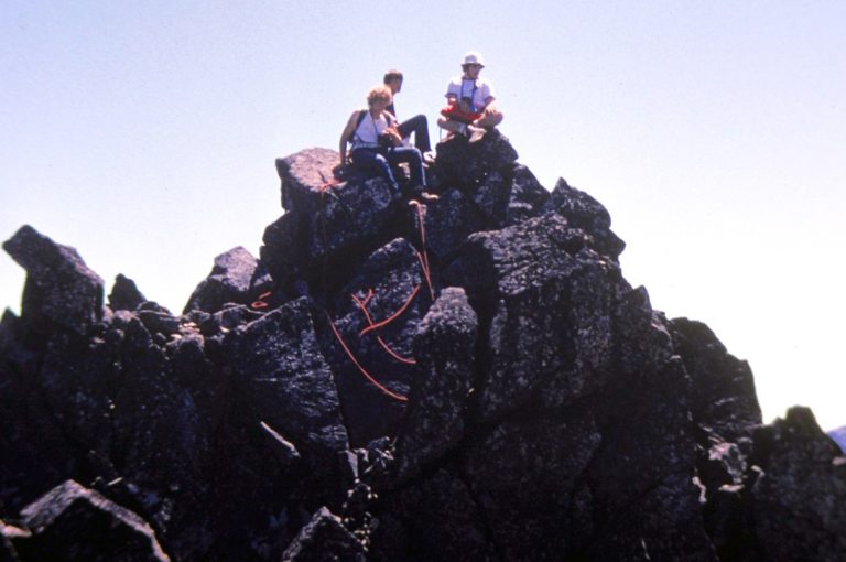 Three mountain climbers sit on the rocky summit of Cashmere Mountain