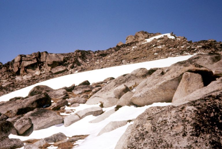 The summit of Colchuck Peak rises above lingering snow patches and cliff bands
