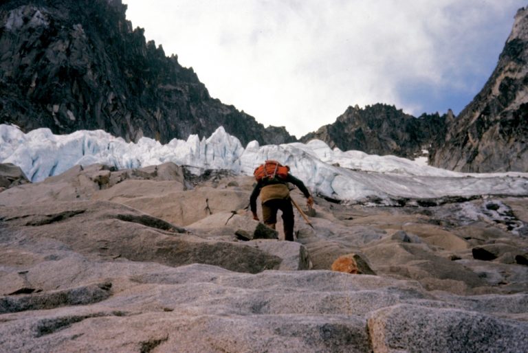 A mountain climber scrambling steep rock slabs which lead to the Sherpa Glacier on Mt Stuart in the Icicle Mountains