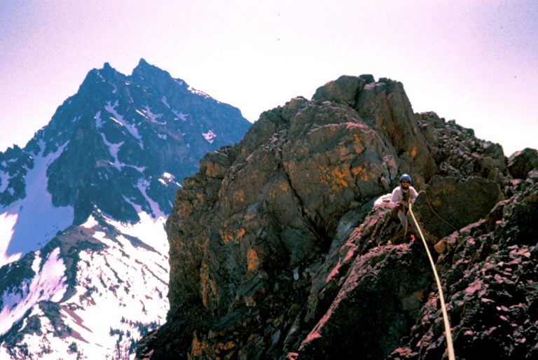 A rock climber belays his partner on East Ingalls Peak in the Teanaway Mountains with Mt Stuart behind