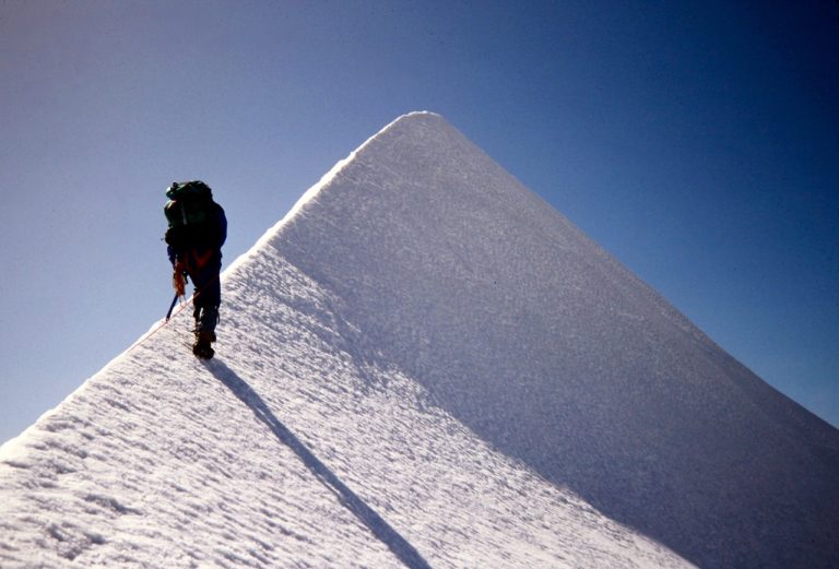 A mountain climber ascends a dramatically steep snow ridge on Eldorado Peak in the North Cascades