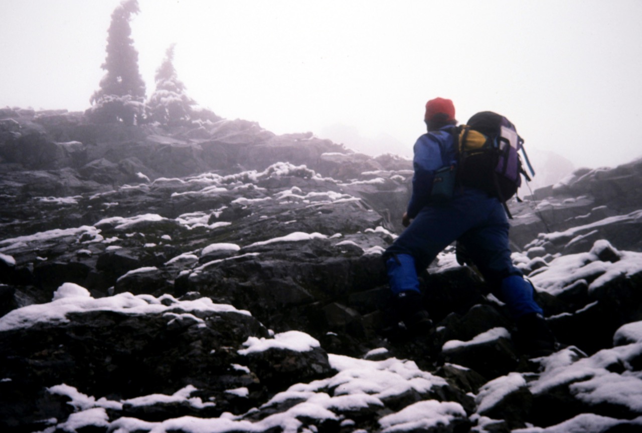 A mountain climber ascends a snow-dusted rock face on Chair Peak
