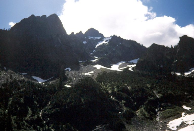 Puffy white clouds sit over the top of craggy Morning Star Peak in the Monte Cristo Mountains