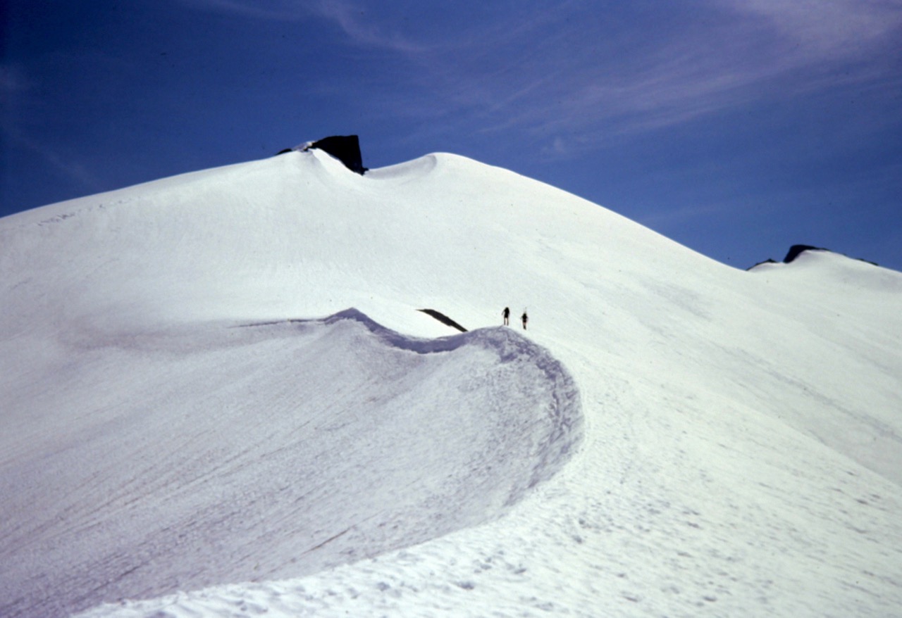 Two climbers ascend a snowy ridge crest on Ruth Mountain in the Nooksack Mountains