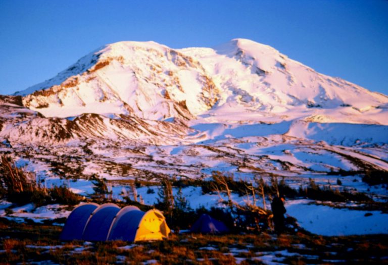Fresh snow covers Mt. Adams as viewed from a green meadow with a blue tent
