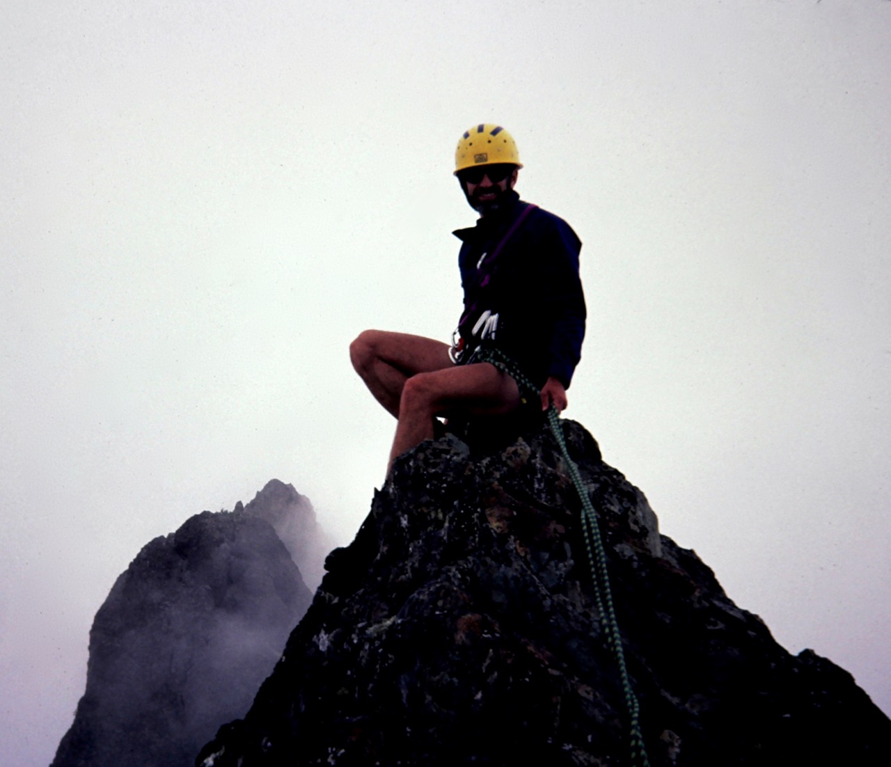 A rock climber sits on the tiny summit of Mt Cruiser