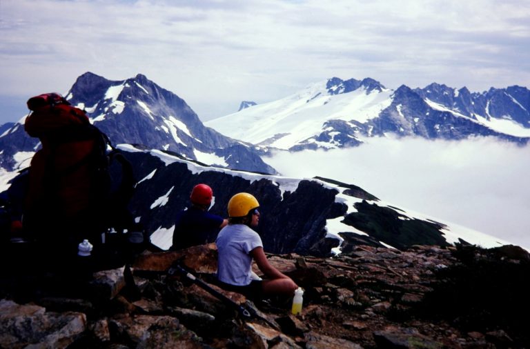 Climbers sit on the summit of Easy Peak and watch Mt Challenger rise above fog in the Northern Pickets
