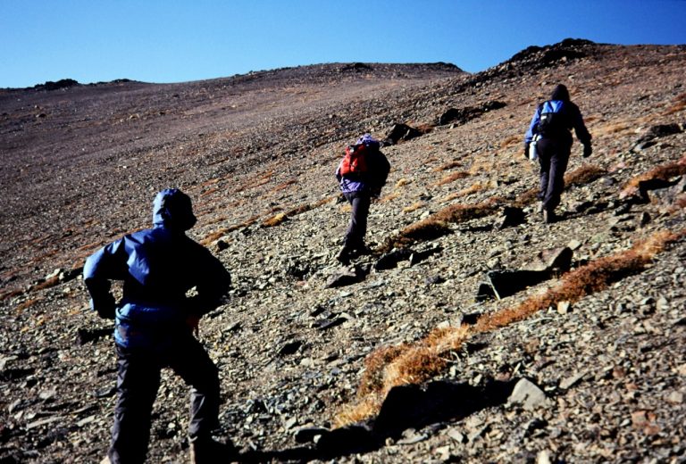 Three hikers scramble up a long rocky slope on Gardner Mtn
