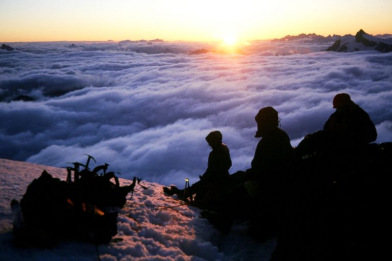 Three mountain climbers watch the sunrise from Mt Baker