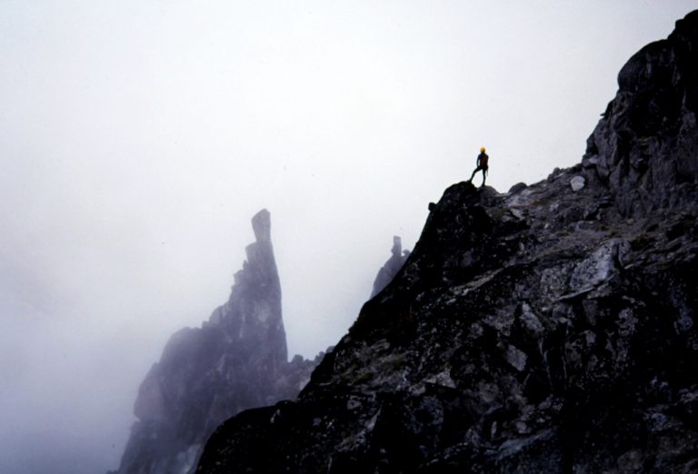 A solitary climber stands atop a jagged ridge on McClellan Peak in The Enchantments