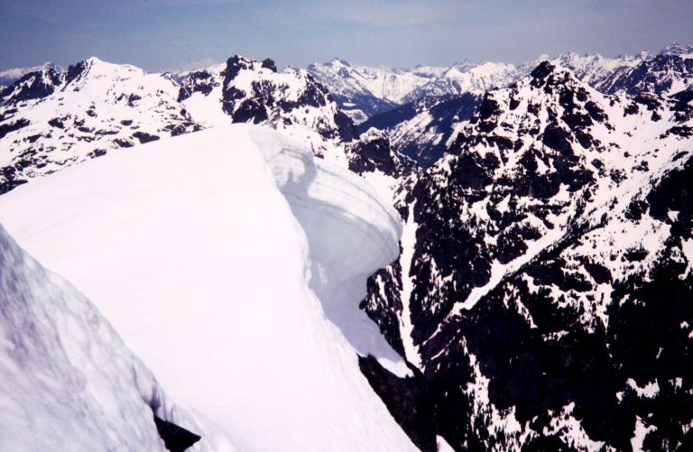 A large snow cornice overhangs a vertical cliff on Mt Baring