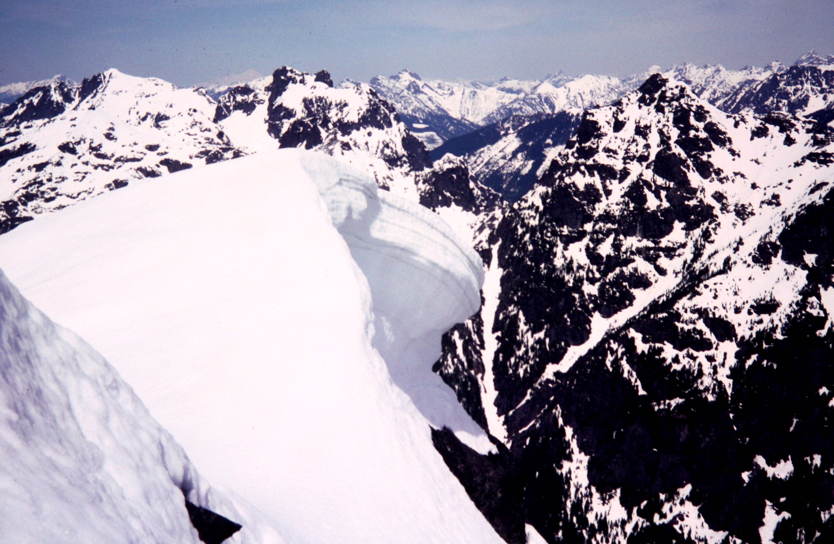 A large snow cornice overhangs a vertical cliff on Mt Baring