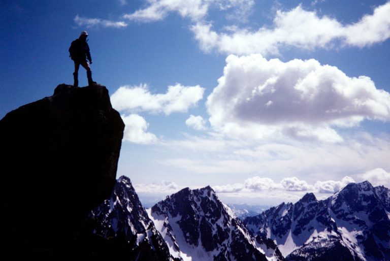 A mountain climber stands atop the summit horn of Cannon Mountain overlooking Stuart Range