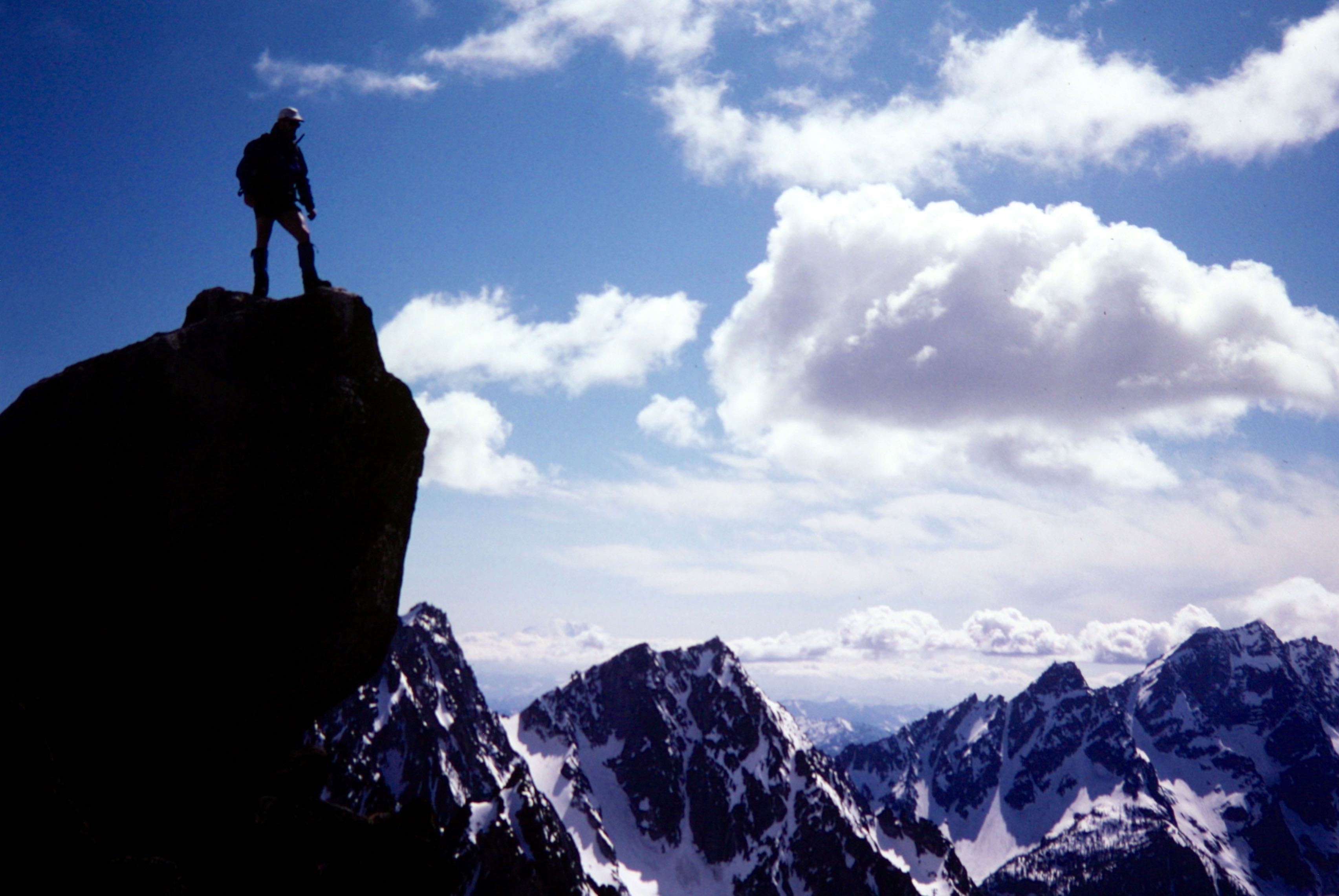 A mountain climber stands atop the summit horn of Cannon Mountain overlooking Stuart Range