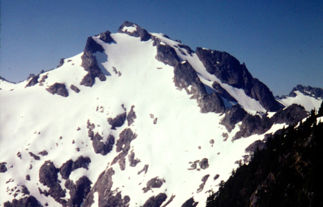 The snowy and rocky summit of Black Mtn stands against a blue sky in the Glacier Peak Wilderness