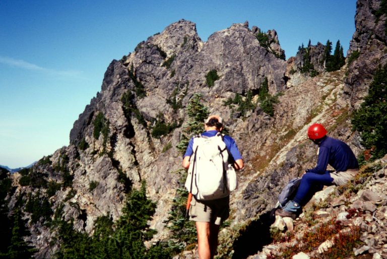 Two mountain climbers study a map below the rocky face of Malachite Peak
