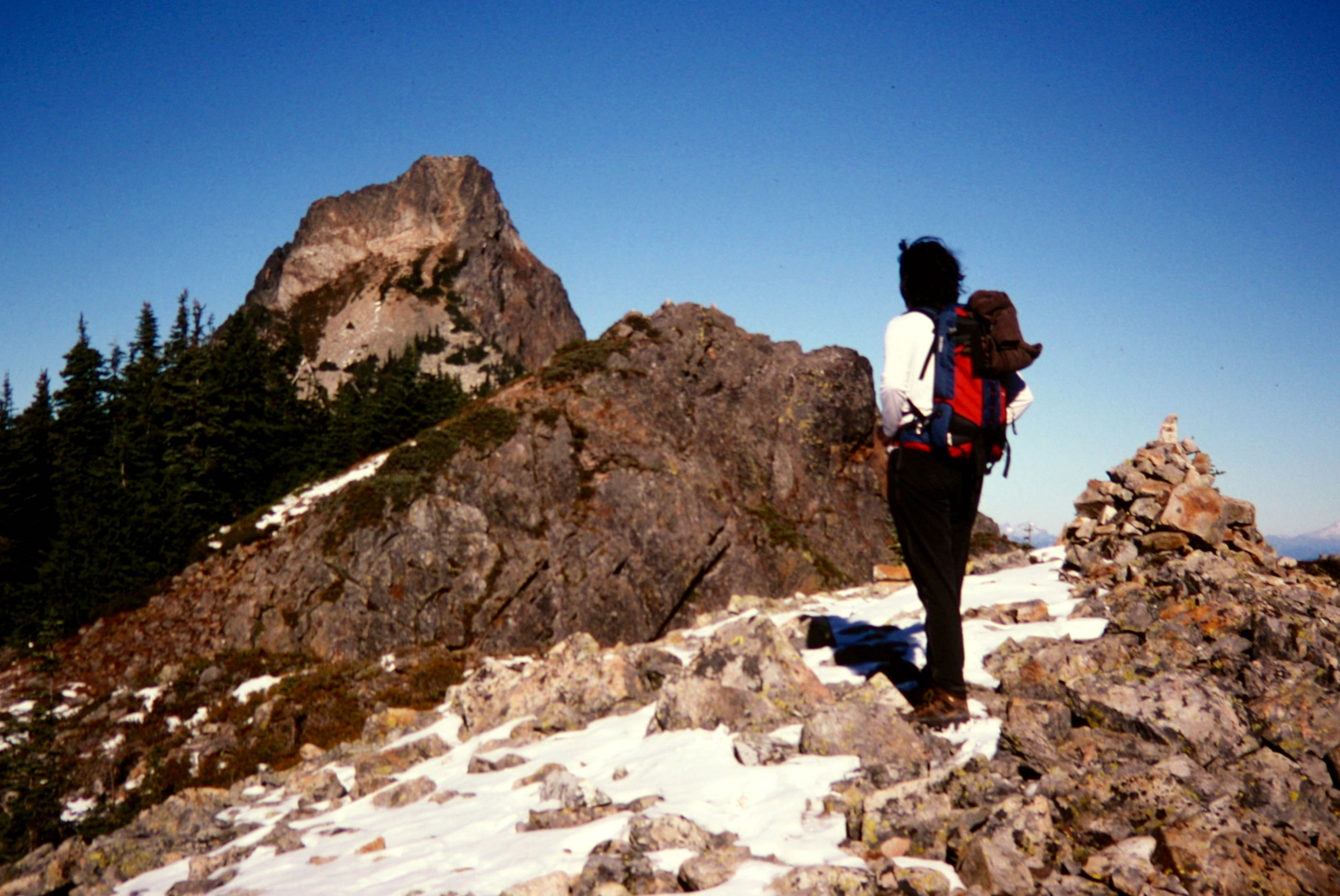 A solo hiker stands on a rocky hill to gaze at Kaleetan Peak