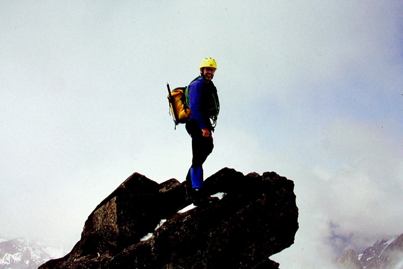 mountain climber stands on the rock horn summit of Austera Peak in the McAllister Mountains with swirling clouds
