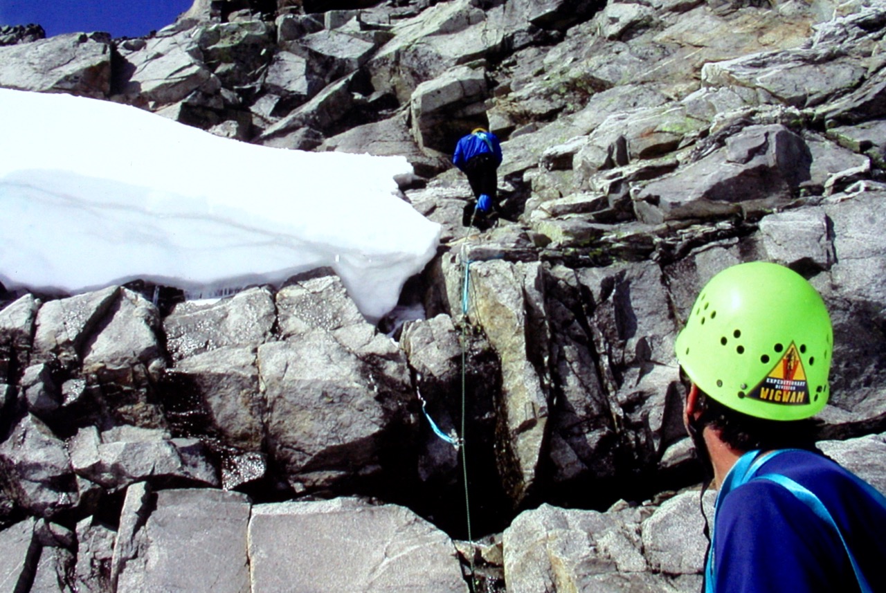 roped mountain climbers leading up broken rock next to linguring snow on Klawatti Peak in the McAllister Mountains