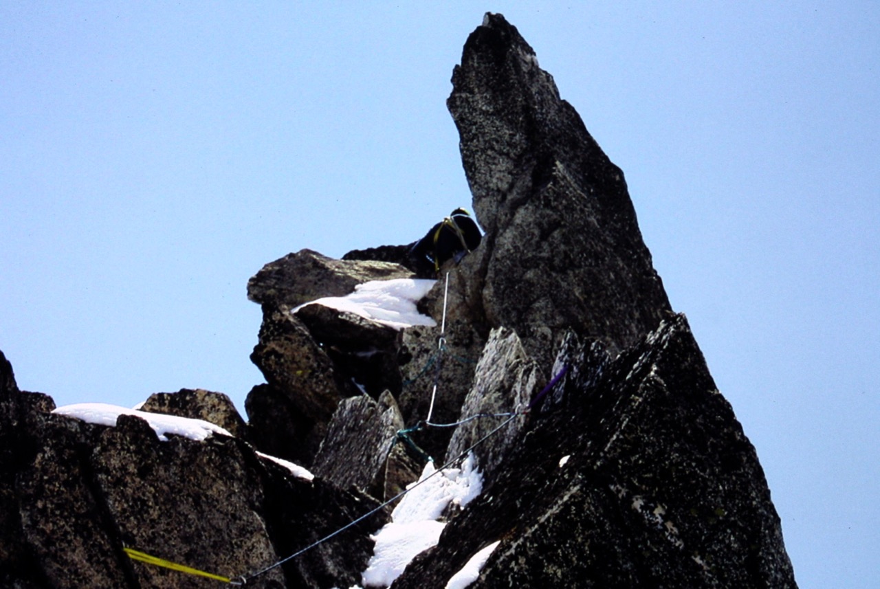 roped mountain climber carefully leads final pitch avoiding linguring snow patches on the summit of Dorado Needle on the Inspiration Traverse in the North Cascades