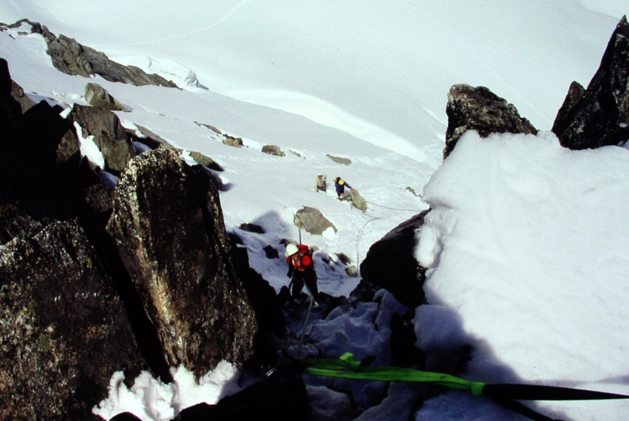 looking down on mountain climber rappelling off the summit of Dorado Needle in the North Cascades with steep snow fields below