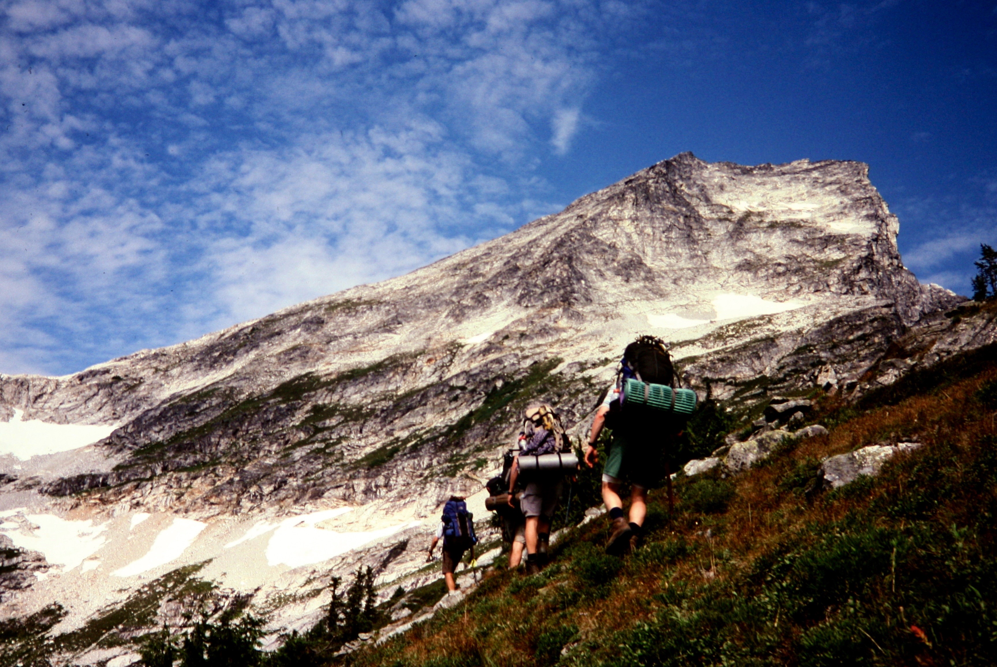 mountain climbers traverse grassy slopes below rocky Luna Peak in the Northern PIckets