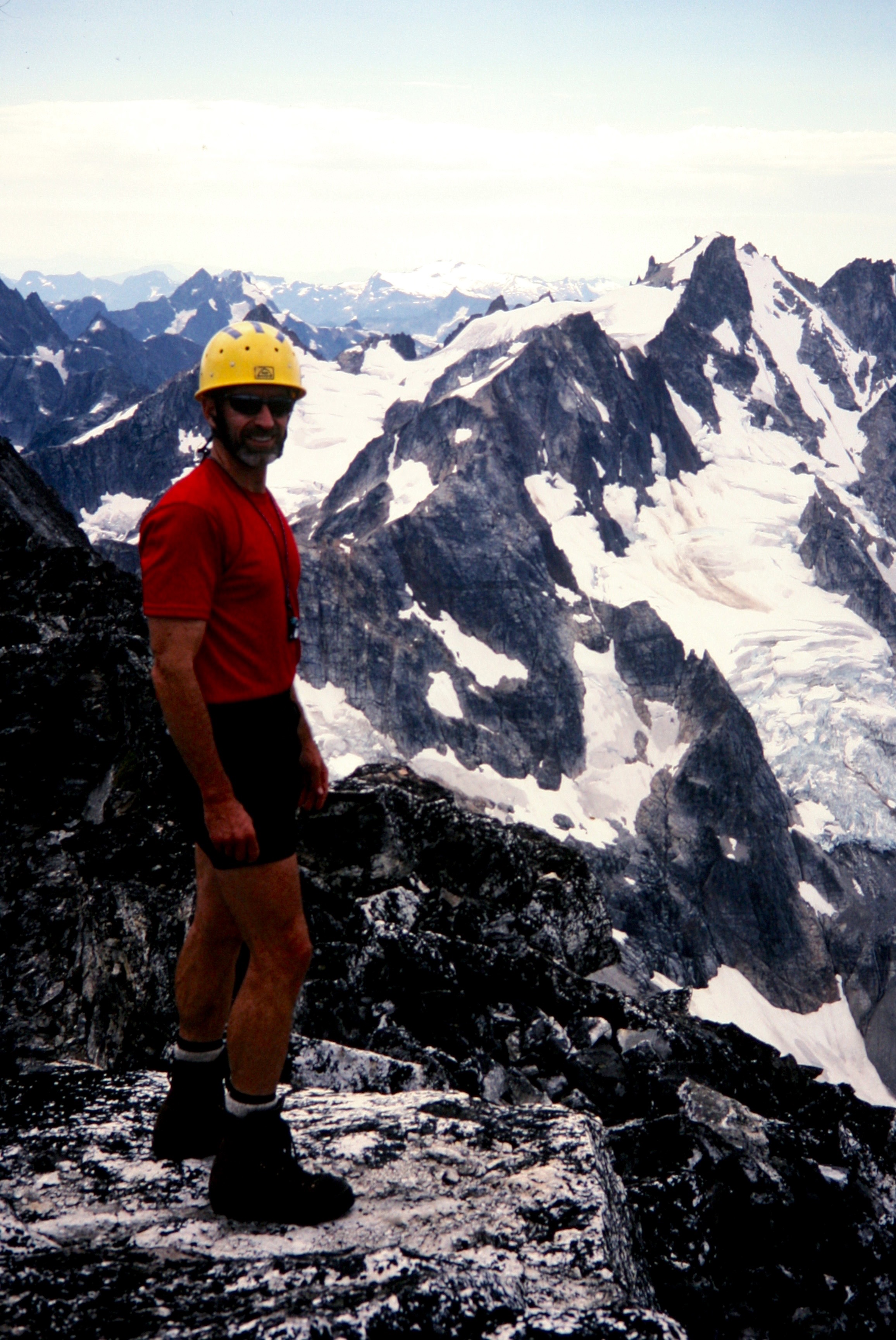 lone mountain climber standing on rock slab at Luna Peak false summit with Mt Fury in the background in the Northern PIckets