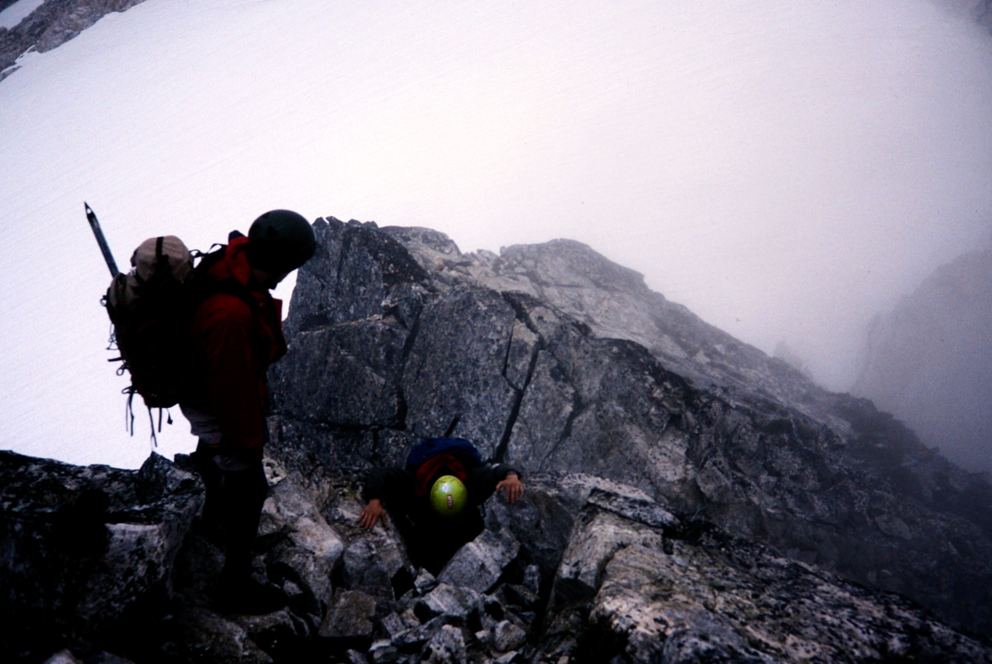 looking down on mountain climbers scrambling the ridge line of Mt Fury with fog swirling around