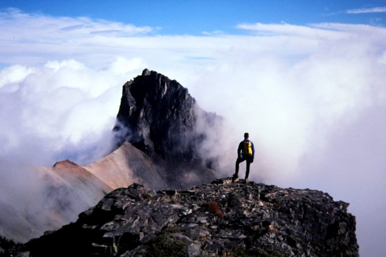 Main Cowlitz Chimney and a lone climber stand silhouetted against white clouds in Mt Rainier National Park