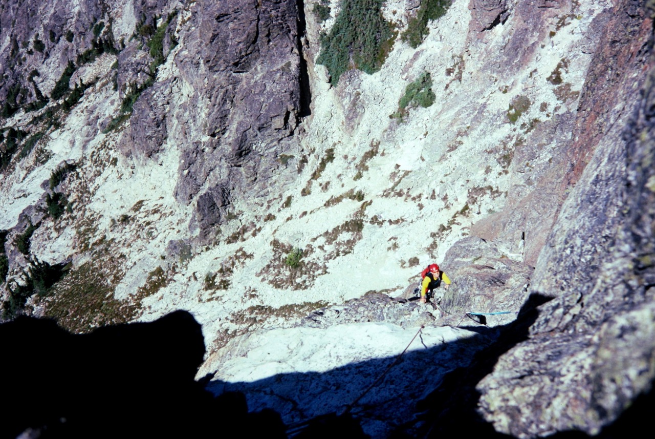 looking down on roped mountain climber working up the crux of the summit tower on Bears Breast Mountain in the Alpine Lakes Wilderness with the steep rock face below