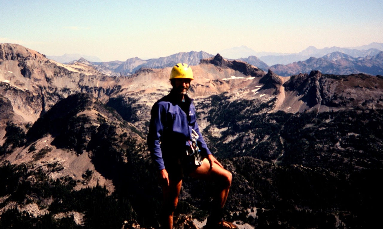 mountain climber on the summit of Bears Breast Mountain with distant views of the Alpine Lakes WIlderness in the background