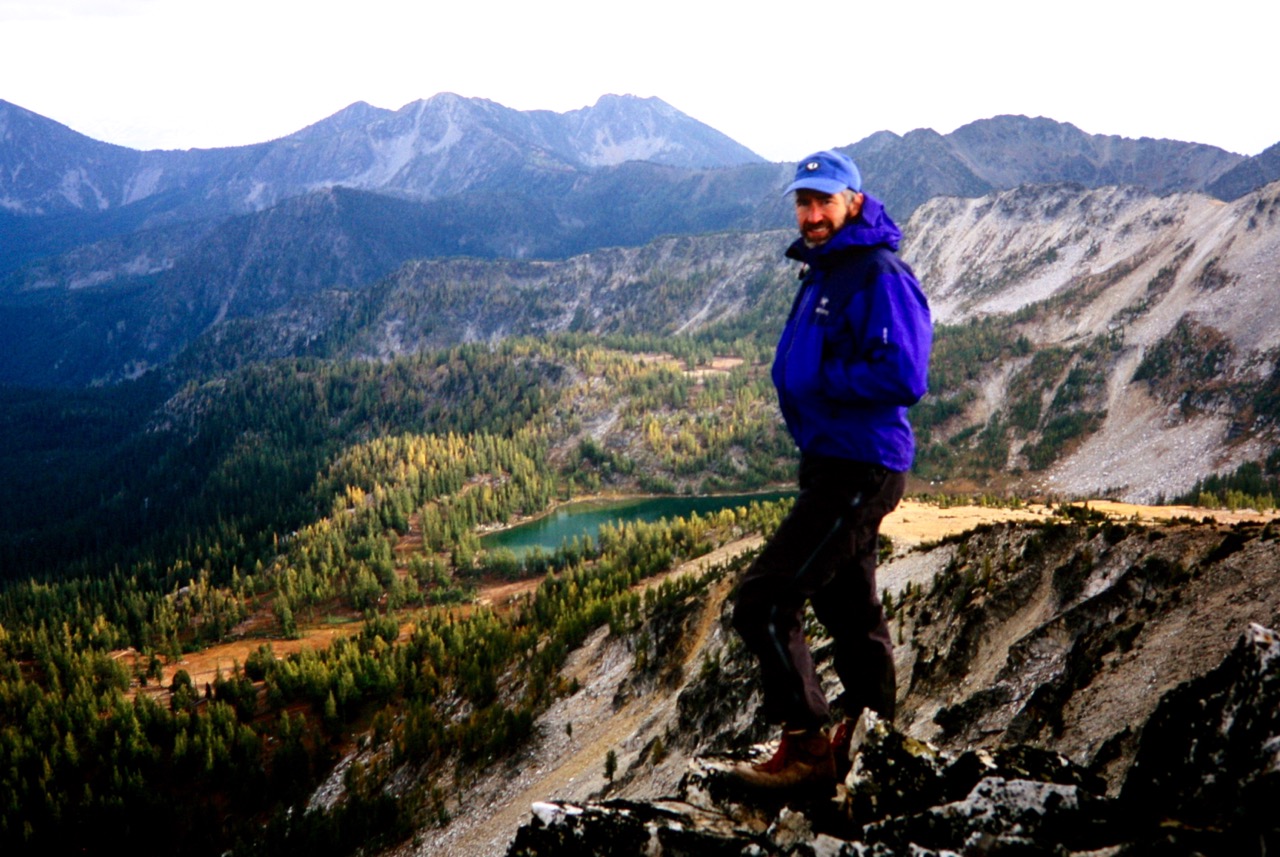 A blue clad climber stands on the summit of Martin Peak in the Sawtooth Mountains