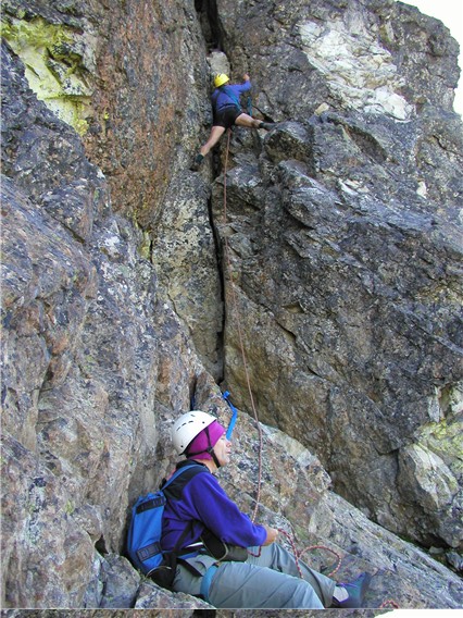mountain climber placing protection as they climb the Dihedral on the summit tower of Bears Breast Mountain in the Alpine Lakes Wilderness