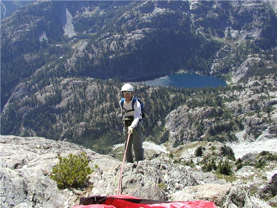 mountain climber rappelling off the summit of Bears Breast Mountain in the Alpine Lakes WIlderness with the rolling, slabby valley bottom in the background