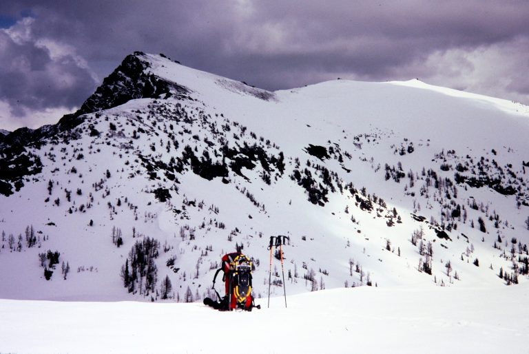 Snow-covered Big Lou Mountain stands behind a snowy ridge with a red backpack