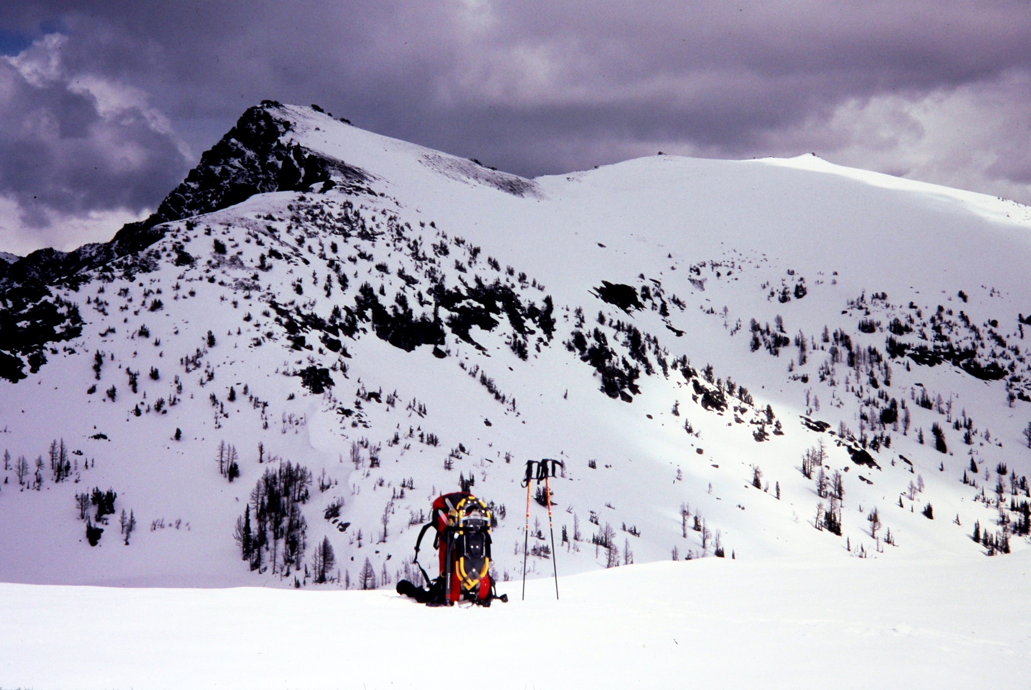 Snow-covered Big Lou Mountain stands behind a snowy ridge with a red backpack