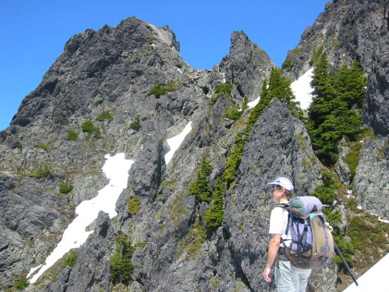 A climber pauses below the gray rocky summit of South Gemini Peak