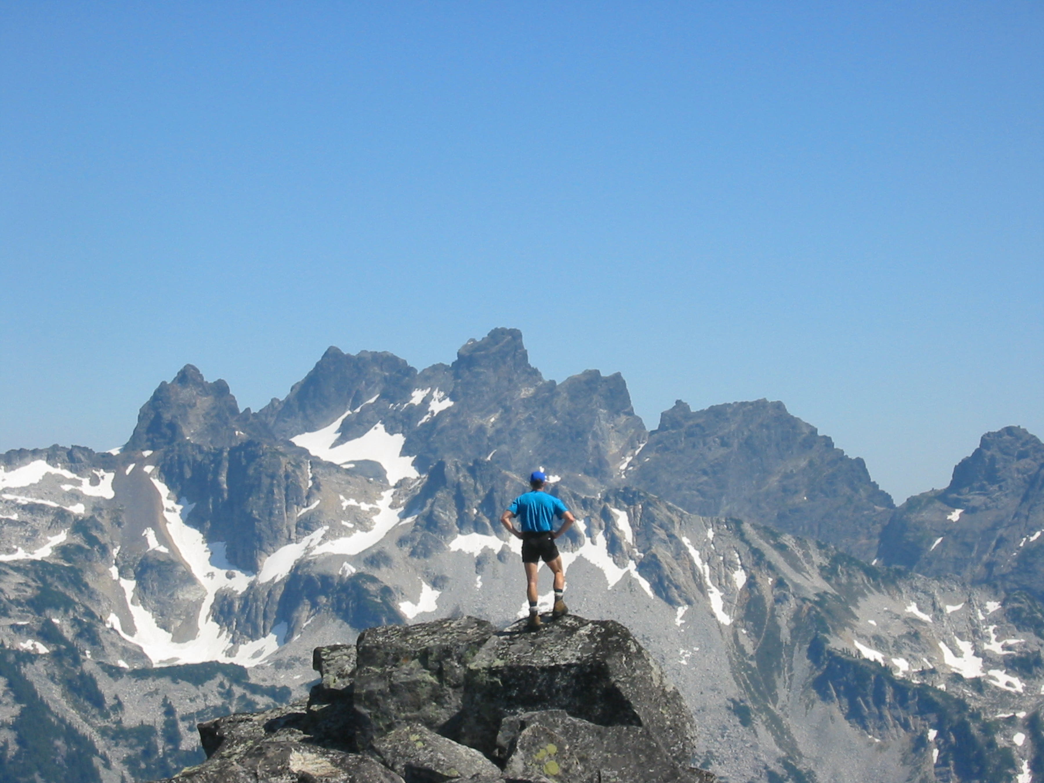 A climber stands on the summit of Big Snow Mountain with Chimney Rock in the background in teh Miller-Foss Mountains