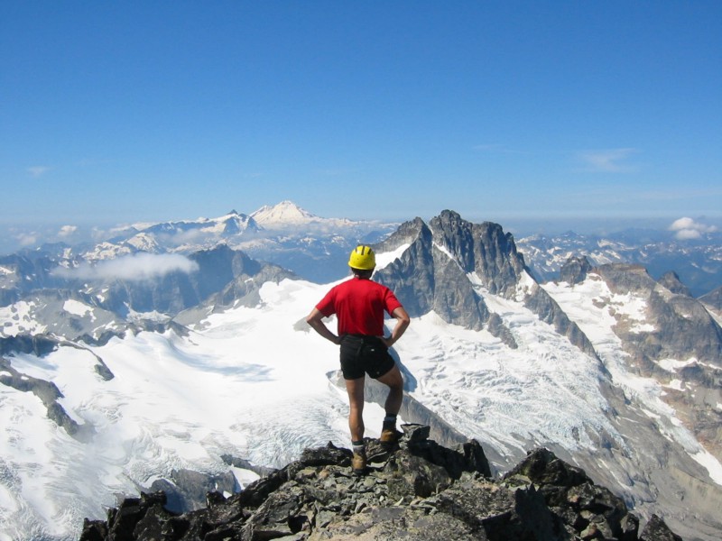lone mountain climber stands on the summit of Mt Spickard looking at Mt Redoubt in the American Chilliwack Mountains