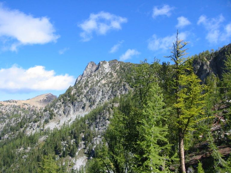 The rocky summit of Choral Peak rises toward a blue sky with clouds