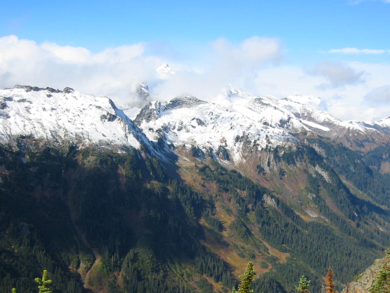 Clark Mountain in the Chiwawa Mountains engulfed in clouds with a valley floor filled with evergreen trees as seen from Little Giant Pass in the Glacier Peak Wilderness