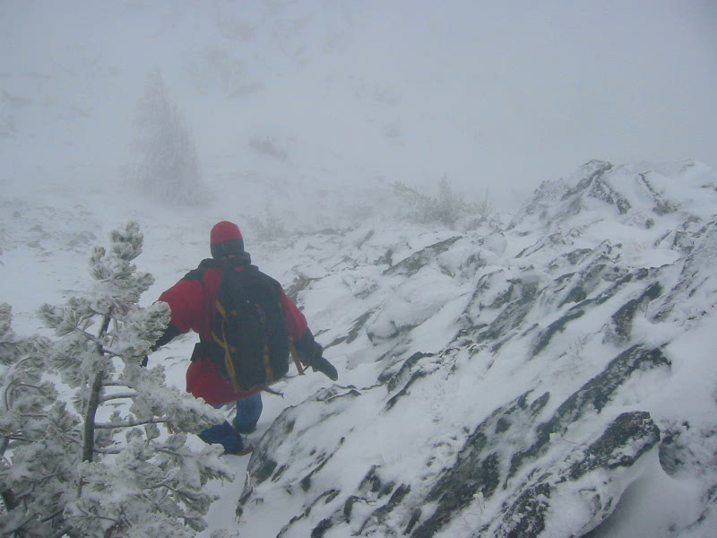 A climber descends a snowy and rocky gully on Devils Smoke Stack