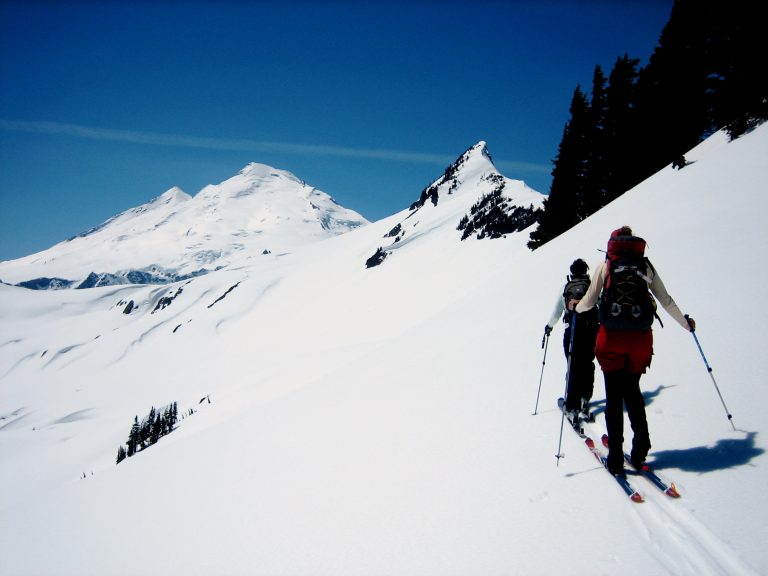 Two backcountry skiers glide along Ptarmigan Ridge toward tooth-shaped Coleman Pinnacle