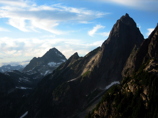 Mt Despair in the Lower Skagit Mountains sits in the distance with high clouds with Mt Triumph in North Cascades National Park in the foreground with randow small snow fields