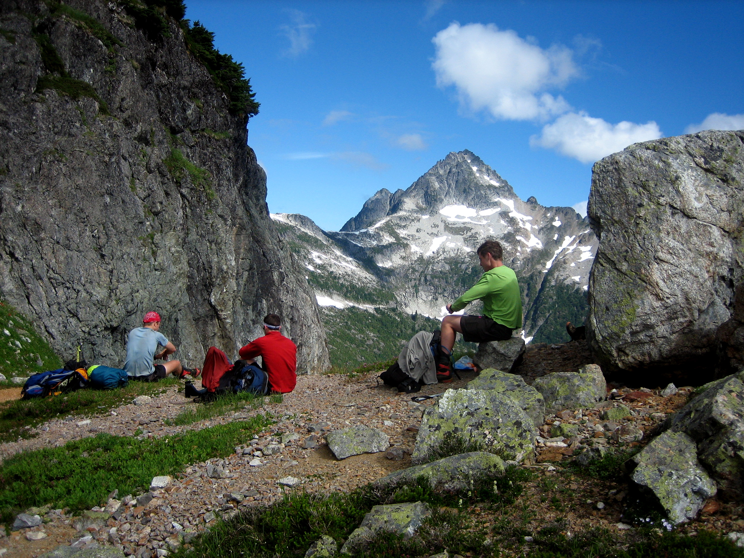 mountain climbers taking a break in the rocks at Triumph Pass in the Lower Skagit Mountains with Mt Despair in North Cascades National Park in the background and puffy clouds
