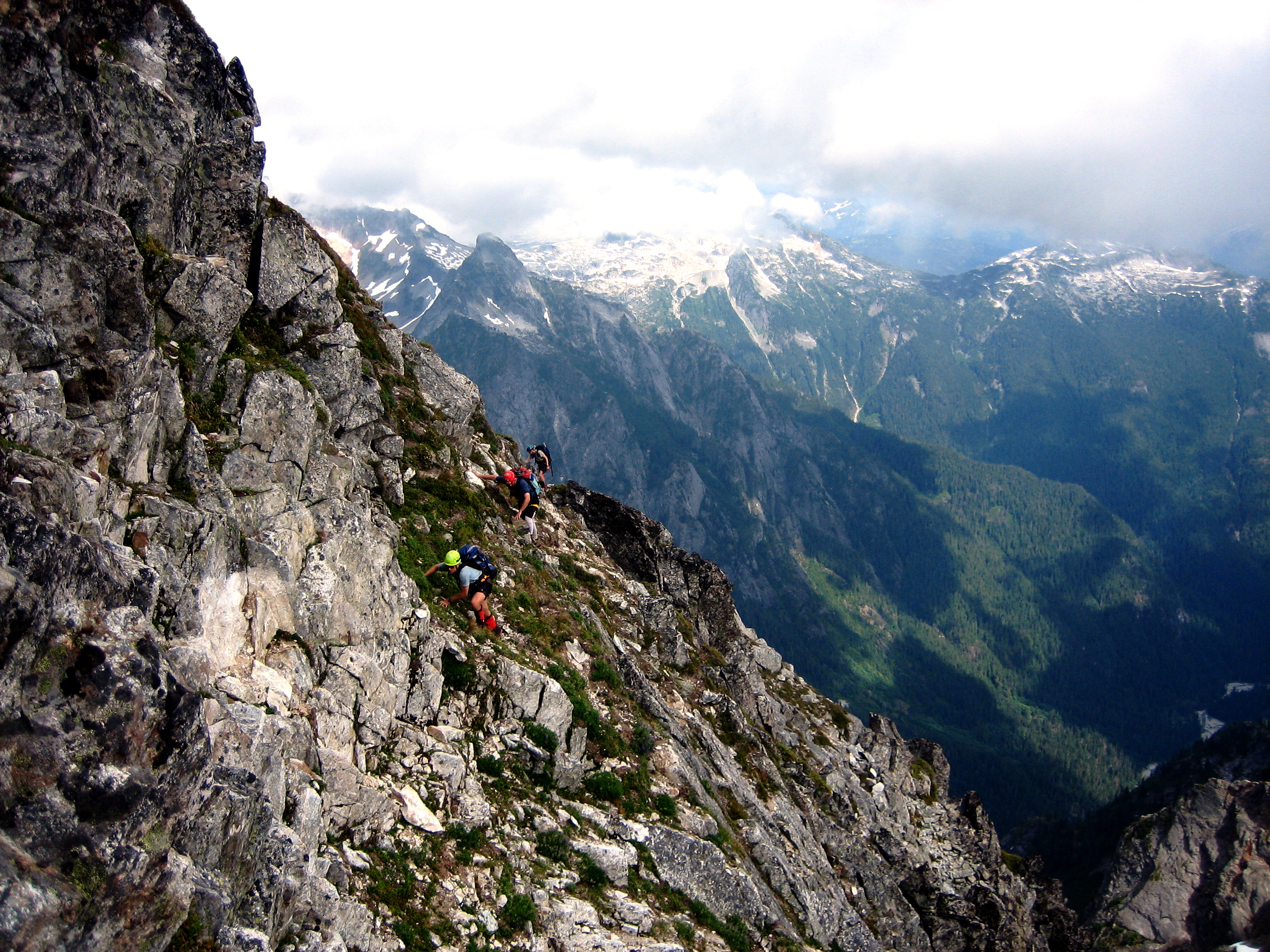 mountain climbers scrambling steep rock and heather on Mt Despair in the Lower Skagit Mountains in North Cascades National Park