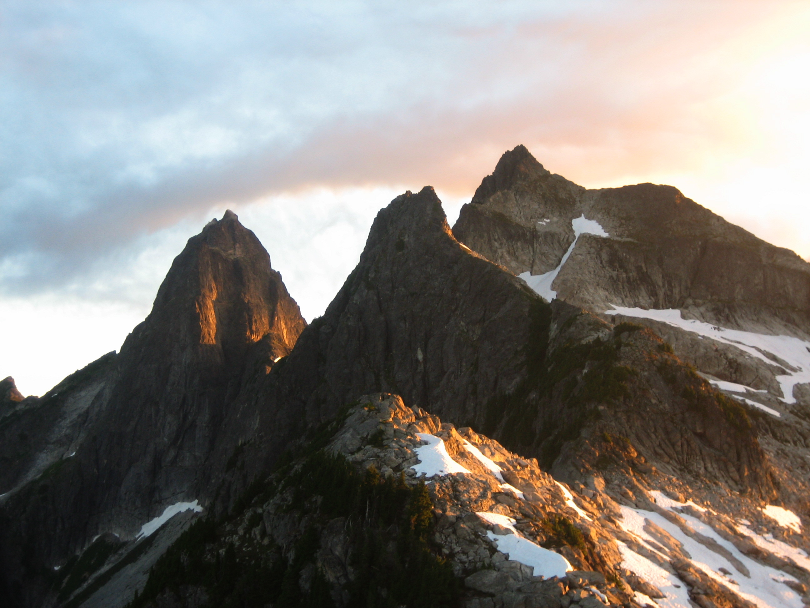 Sunrise on the three rock horns that make up Mt Triumph with linguring snow patches in the Lower Skagit Mountains in North Cascades National Park